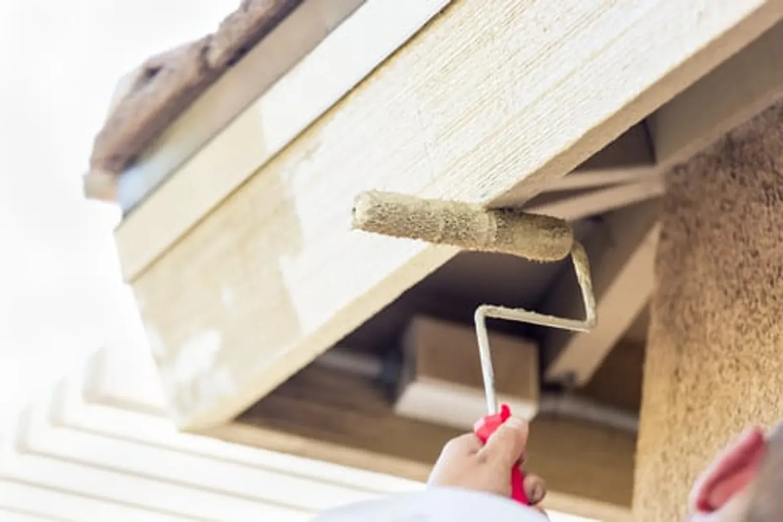Painter rolling fresh paint onto the eaves and fascia of a house exterior